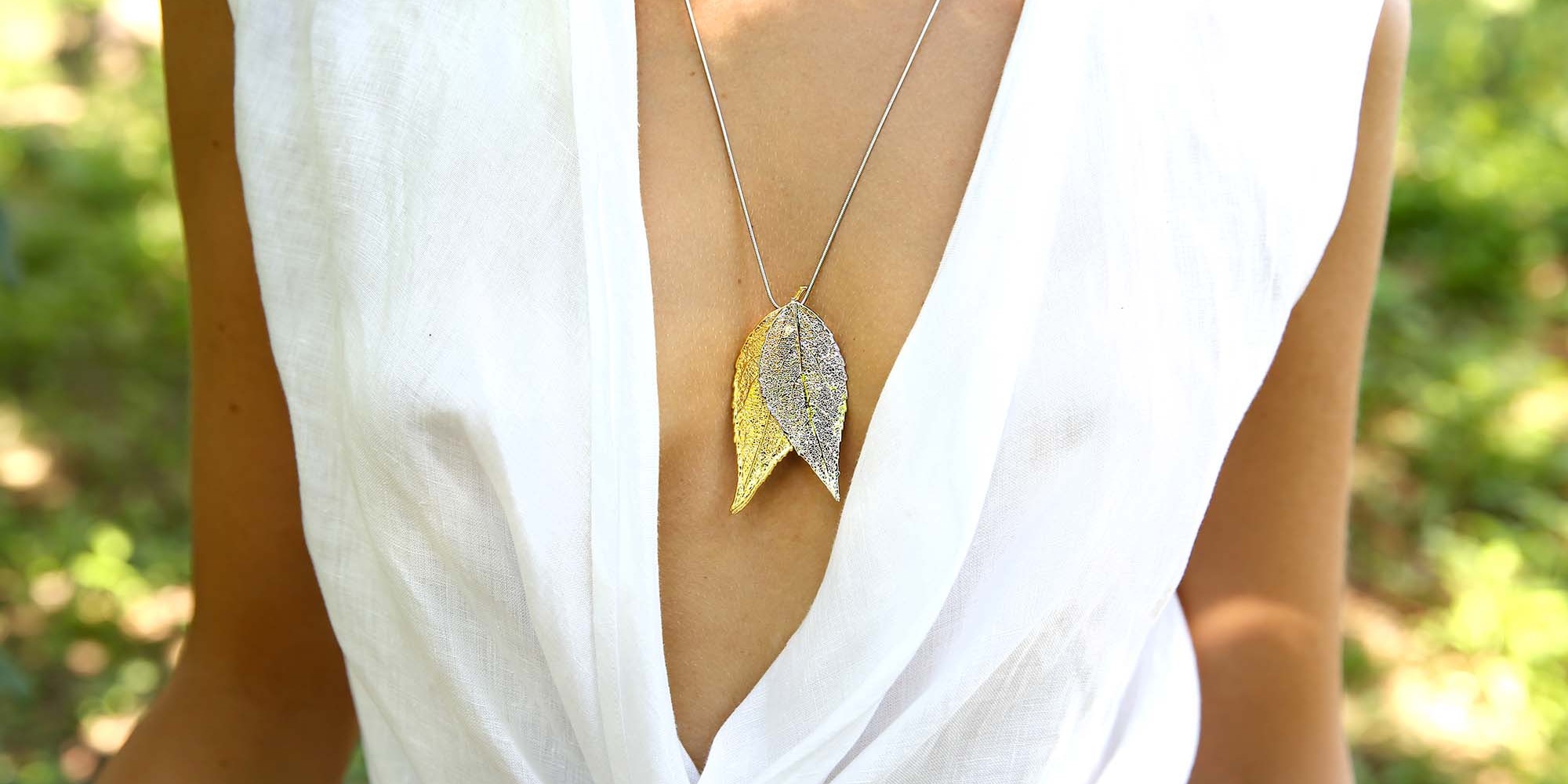 Ciondolo indossato da modella con due vere foglie di ciliegio una placcata oro e l'altra argento