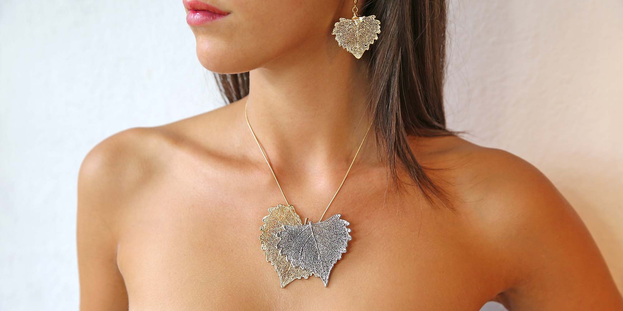 Parure indossata da modella di orecchini di vere foglie di cotone placcate argento e ciondolo due toni con due foglie di cotone una placcata oro e l'altra argento